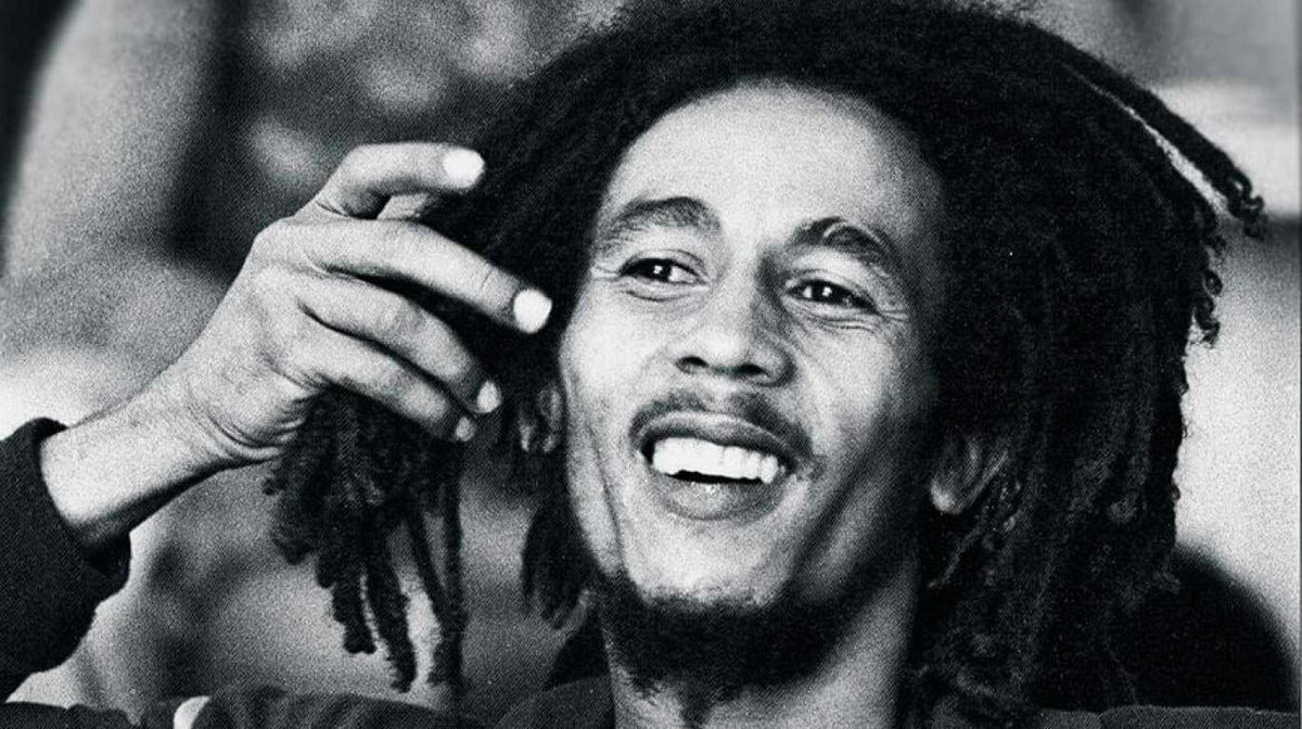 Portrait en noir et blanc de Bob Marley souriant, la main près de ses dreadlocks