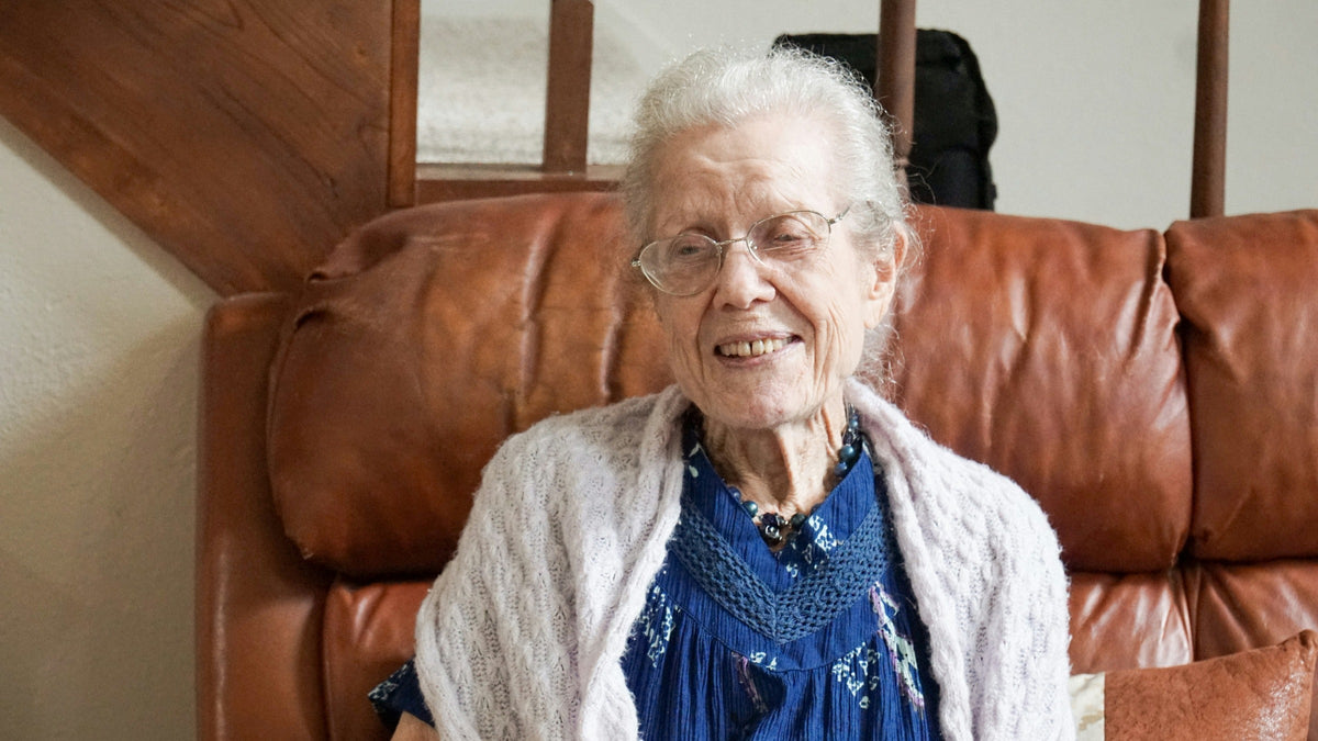 Femme âgée souriante portant des lunettes, un cardigan clair et un collier bleu Image