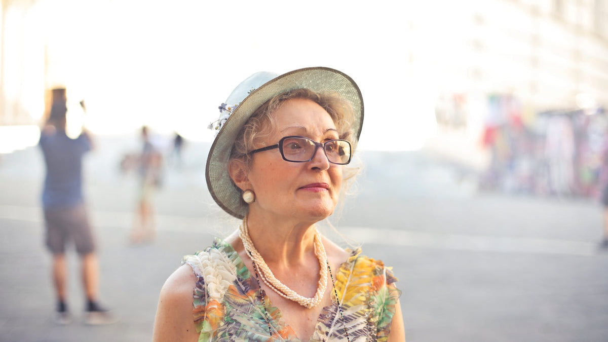 Femme de plus de 60 ans portant lunettes, rouge à lèvres rose, chapeau et collier perlé Image